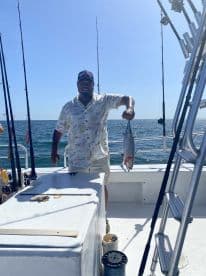 An angler proudly displaying a caught fish aboard a fishing boat in open waters, showcasing a successful day of deep-sea fishing.