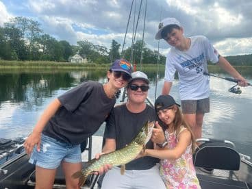 A family enjoying a successful fishing trip, showcasing a Northern Pike caught on a scenic lake.
