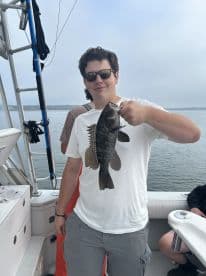 Angler proudly displaying a large Black Bass while fishing on a boat, showcasing a successful day on the water.