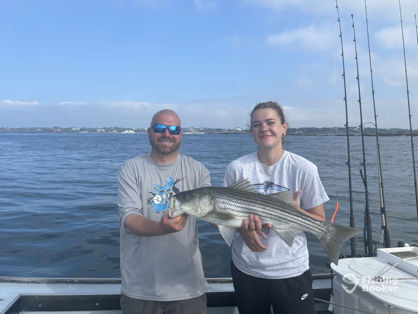 A young angler and an adult proudly displaying a large Striped Bass while fishing on a calm day.