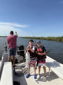 Two young anglers proudly displaying a large catfish while fishing on a boat in a scenic waterway.