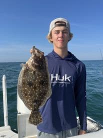 A young angler proudly displaying a Flounder while fishing on a sunny day.