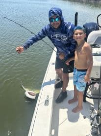 A young boy and an adult are fishing on a boat, with a large fish being reeled in, showcasing an exciting moment on the water.