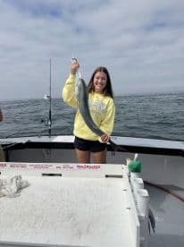 A young woman proudly displaying a large fish while fishing on a boat, showcasing a successful day on the water.