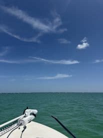 A scenic view from the side of a boat on a clear day, showcasing the turquoise waters and blue sky, perfect for a fishing adventure.