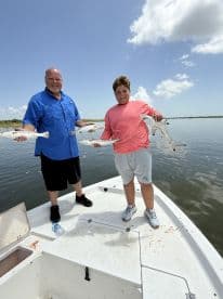 A proud adult and a young angler displaying their catch of Speckled Trout while on a fishing boat in calm waters.
