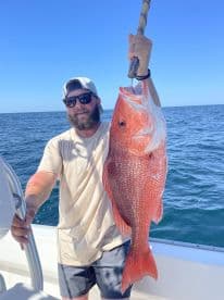 Angler proudly displaying a large Red Snapper while fishing offshore, showcasing a successful day on the water.