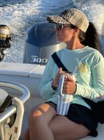 A woman enjoying a relaxing moment on a boat, holding a drink while seated near the helm, with the engine visible in the background.