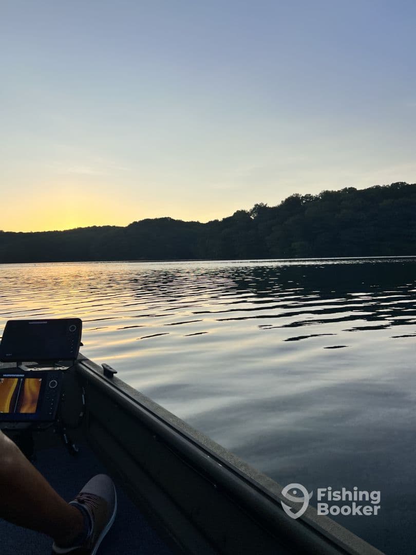 A serene evening view from inside a fishing boat, showcasing the calm waters and electronic fish finder as the sun sets over the horizon.
