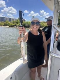A smiling angler proudly displaying a freshly caught Speckled Trout while fishing on a sunny day.