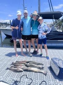 A family of four proudly displaying their catch of speckled trout on a dock after a successful fishing trip.