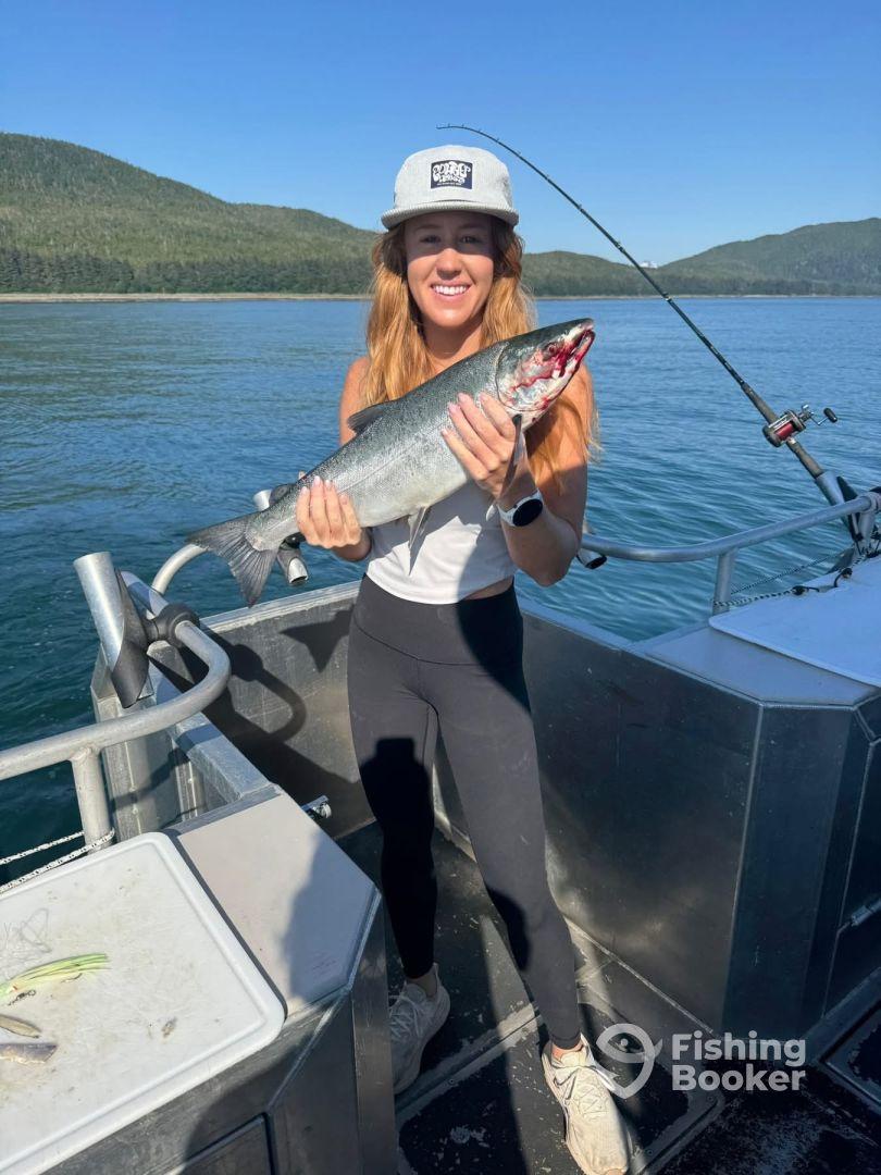 A young woman proudly displaying a freshly caught Salmon while fishing on a scenic boat trip.