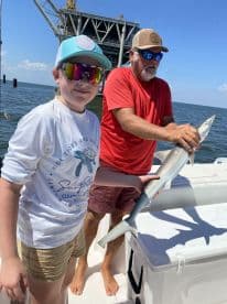 A young angler proudly holding a small shark while fishing near an offshore platform, showcasing a fun day on the water.