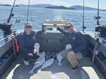 Two anglers proudly displaying their catch of halibut on a fishing boat in a scenic coastal environment.