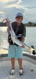 A young angler proudly displaying a caught fish while on a boat, enjoying a sunny day on the water.