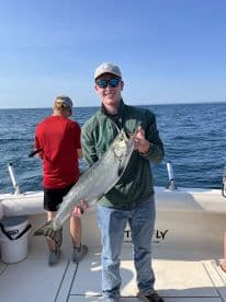 A proud angler displaying a large Salmon while fishing on a charter boat, with another fisherman in the background.