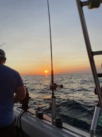 A fisherman is seen preparing to cast a line as the sun sets over the ocean, creating a picturesque backdrop for a fishing adventure.