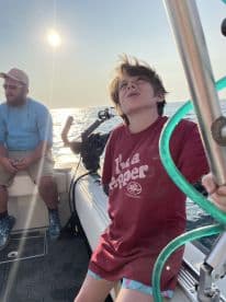A young boy sitting inside a boat, looking up towards the sun, while an adult companion is seated nearby, enjoying a day on the water.