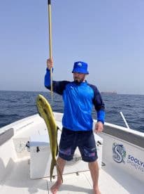Angler proudly displaying a large Mahi Mahi while fishing on a sportfishing boat in open waters.