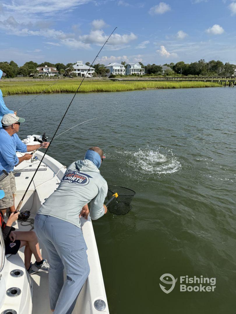 A group of anglers actively fishing from a boat, with one person using a net to catch a fish in a scenic coastal environment.