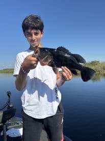 A young angler proudly displaying a large Largemouth Bass while fishing on a serene lake.