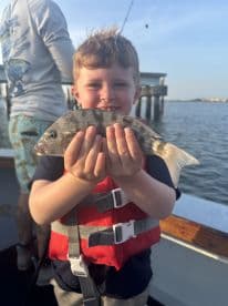 A young angler proudly displaying a caught fish while wearing a life jacket on a fishing trip.