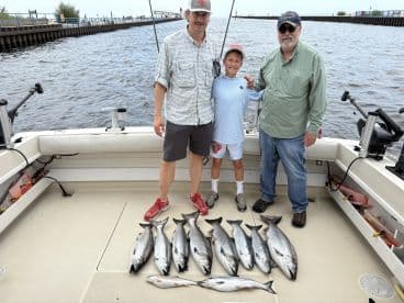 A family group proudly displaying their catch of several Silver Salmon on a fishing charter, with a scenic waterfront in the background.