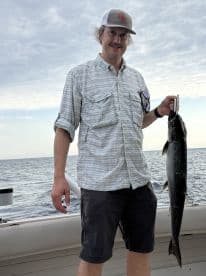 Angler proudly displaying a large fish while aboard a boat, with a scenic ocean backdrop.