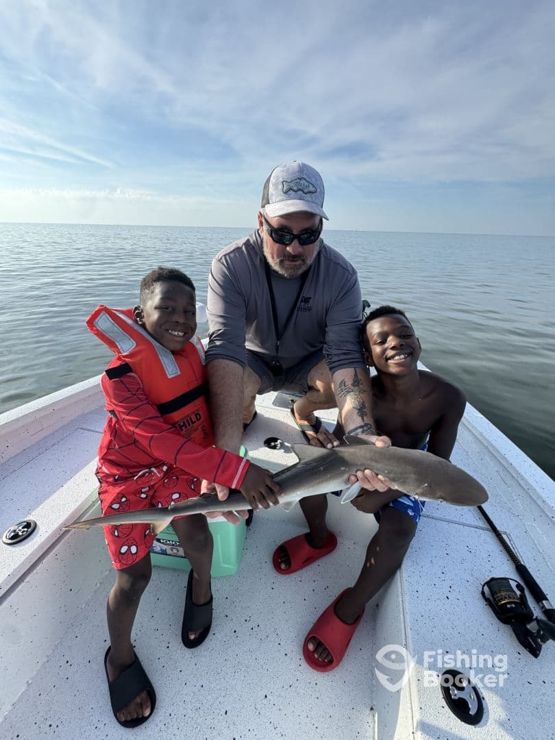 Two young anglers proudly holding a shark while fishing on a boat, showcasing a fun family fishing experience.