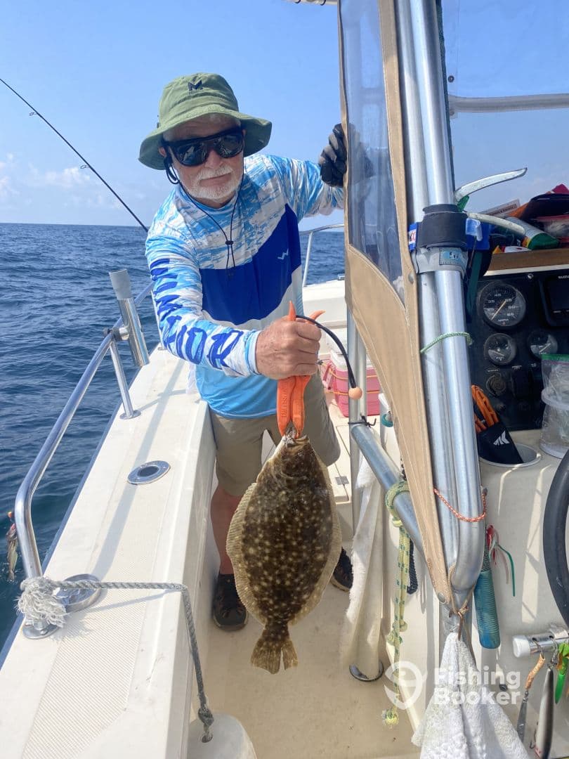 An angler proudly displaying a large Flounder aboard a fishing boat in open waters.