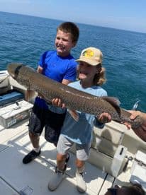 Two young anglers proudly displaying a large fish on a boat during a fishing trip.