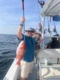 An angler proudly displaying a large Red Snapper while fishing on a charter boat, showcasing a successful day on the water.
