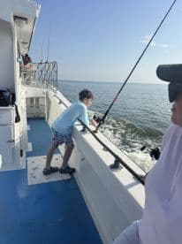 A young angler is focused on fishing from the side of a charter boat, enjoying a sunny day on the water.