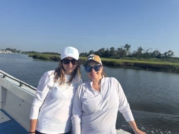 Two women enjoying a scenic day on the water, showcasing the boat's exterior against a lush green backdrop.