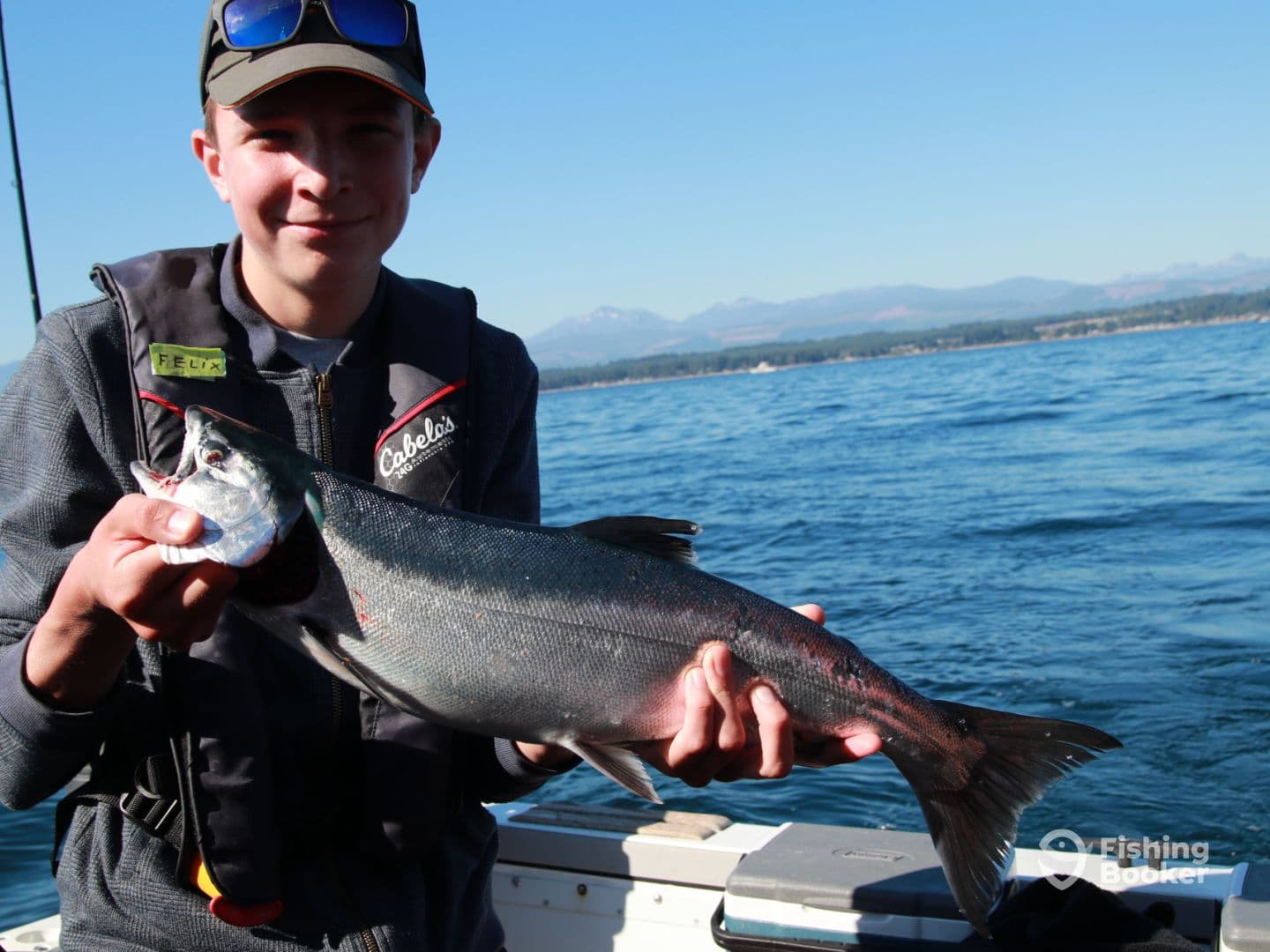 Young angler proudly holding a large salmon while fishing in a scenic coastal environment.