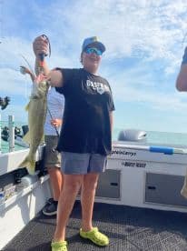 A young angler proudly displaying a Walleye while fishing on a charter boat, showcasing a sunny day on the water.