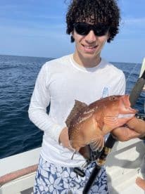 A young angler proudly displaying a colorful Grouper while fishing offshore, showcasing a sunny day on the water.