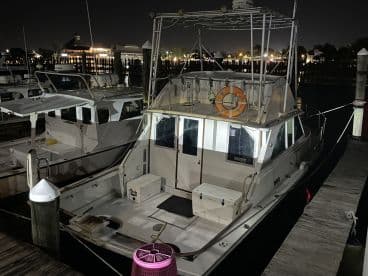 A well-lit exterior view of a fishing boat docked at night, showcasing its design and features against a backdrop of marina lights.