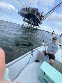 Angler reeling in a catch near an offshore oil rig, showcasing an exciting fishing experience in the Gulf waters.