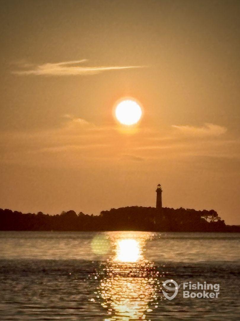A serene sunset view over the water with a lighthouse silhouette, creating a tranquil fishing environment.