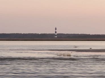 A distant view of a lighthouse at dusk, surrounded by calm waters and a serene landscape.