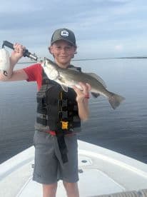 A young angler proudly displaying a Speckled Trout while fishing from a boat in calm waters.