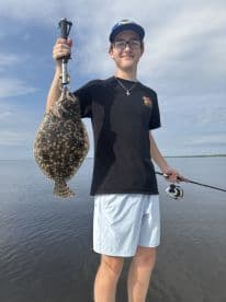 Young angler proudly holding a large Flounder while fishing in calm waters, showcasing a successful catch.