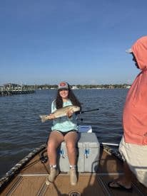 A young angler proudly displaying a Redfish while seated on a boat, enjoying a day of fishing in calm waters.