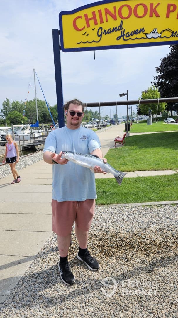 An angler proudly displaying a freshly caught Salmon at Chinook Park in Grand Haven, showcasing a vibrant fishing environment.
