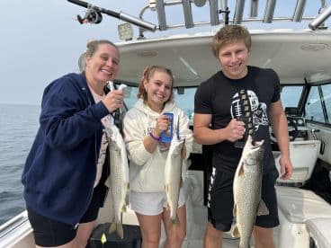 Three anglers proudly displaying their catch of Lake Trout aboard a fishing boat, showcasing a successful day on the water.