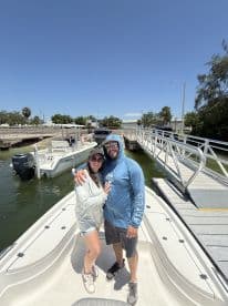A couple poses on the deck of a center console boat at the marina, ready for a day of fishing in sunny weather.