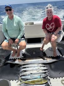 Two anglers sitting on a boat, showcasing a variety of fish including a large Sailfish and several smaller species, after a successful offshore fishing trip.
