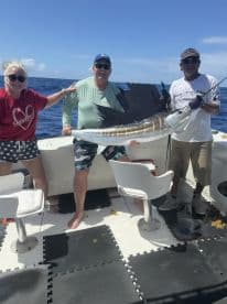 Group of anglers proudly displaying a large Sailfish aboard a fishing boat in open waters.