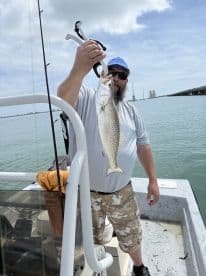 An angler proudly displaying a Speckled Trout while fishing from a boat in coastal waters.